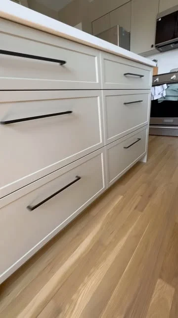 Close view of white slim-shaker drawers and black bar pulls beneath a white kitchen countertop.