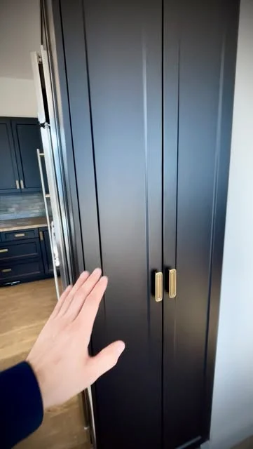 Tall dark blue or charcoal paneled cabinet doors with brass handles and a hand showing the finish.